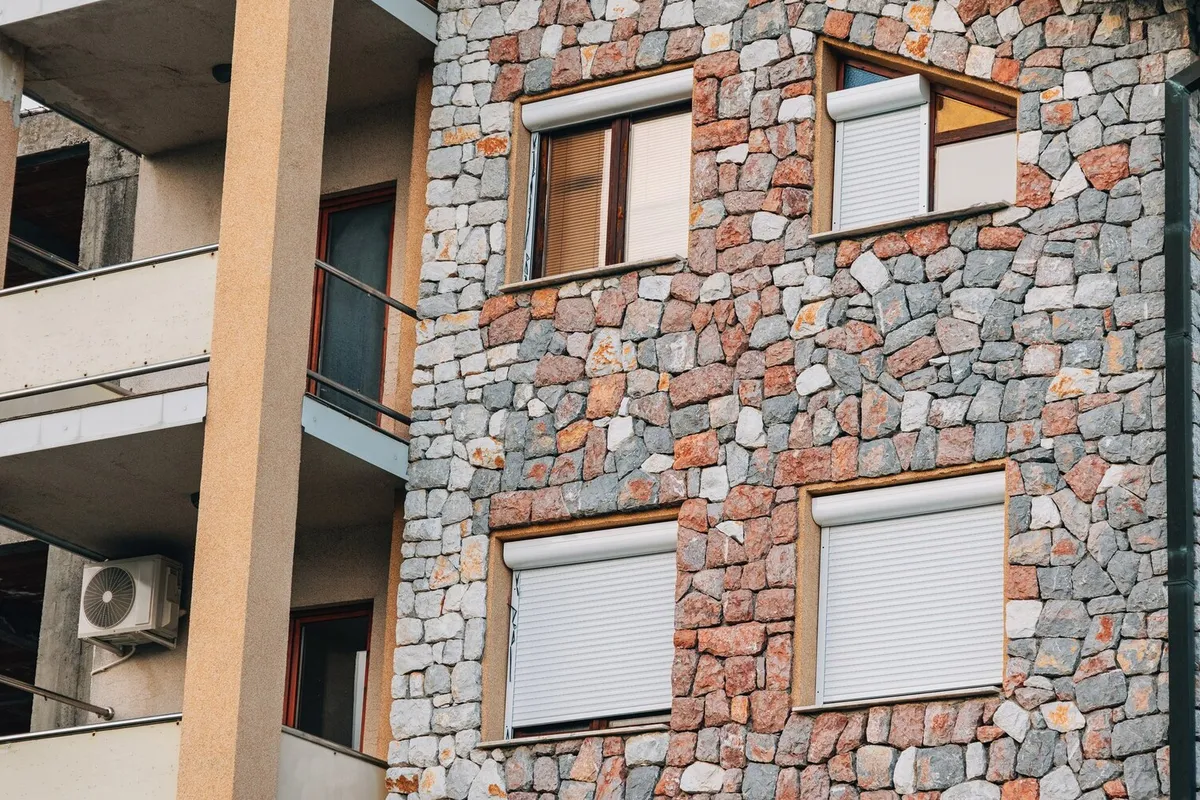 Volets roulants blancs et leurs coffres sur la façade en moellons de pierre d'un immeuble d'habitation